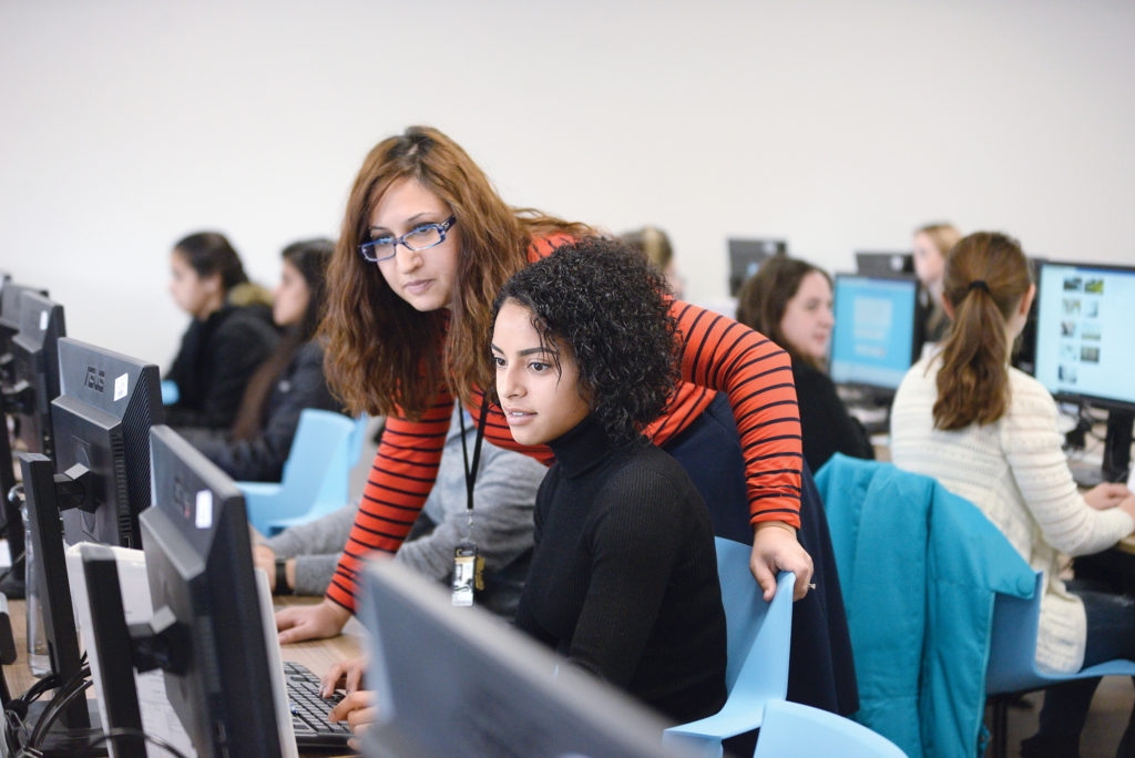 Office Administration Legal instructor works with a student at a computer in-class.