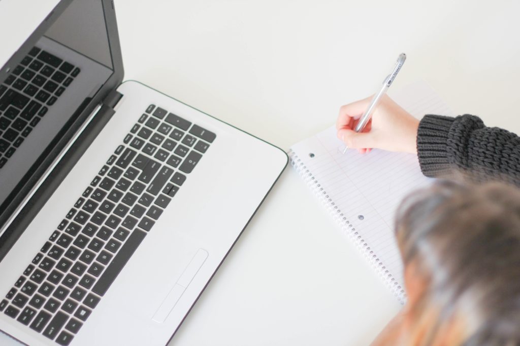 A person writing notes on a pad of paper next to a laptop.