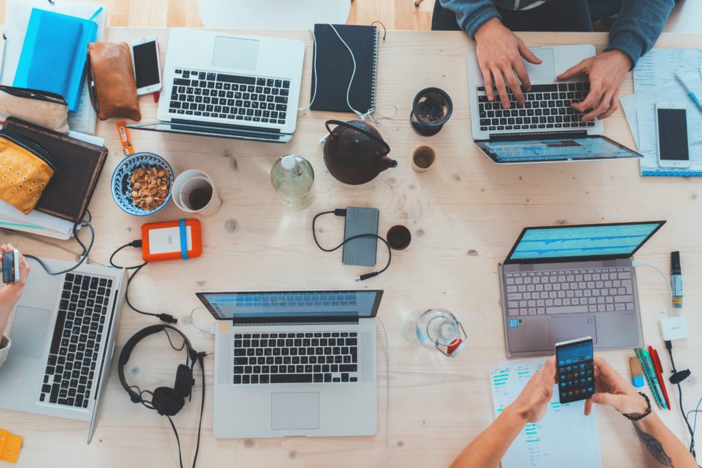 laptops and devices all over a work surface, with hands interacting with them