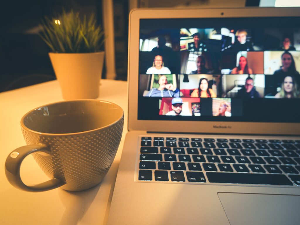 A Zoom meeting going over a laptop placed on a table with mug places in side and planter out of focus in background.