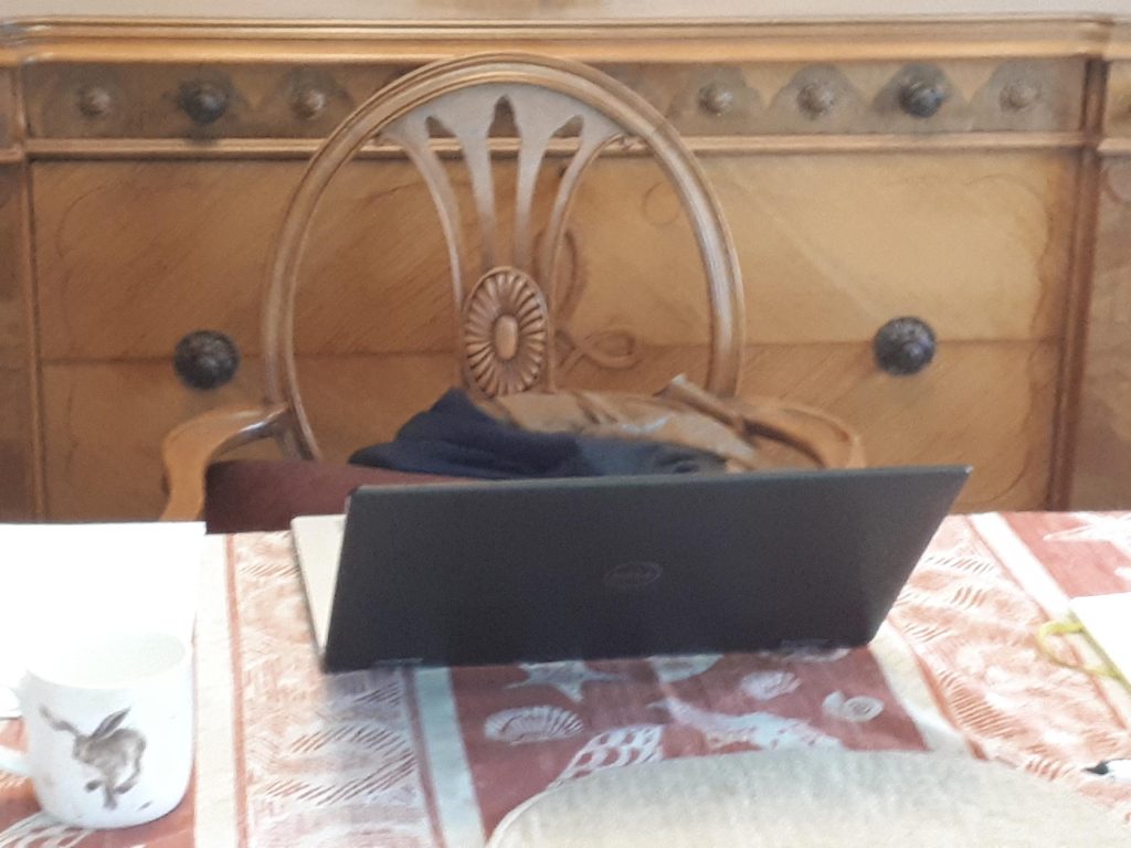 A laptop on a table with a chair and a cup
