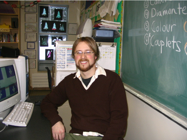Joel Baupre at a computer desk near a blackboard