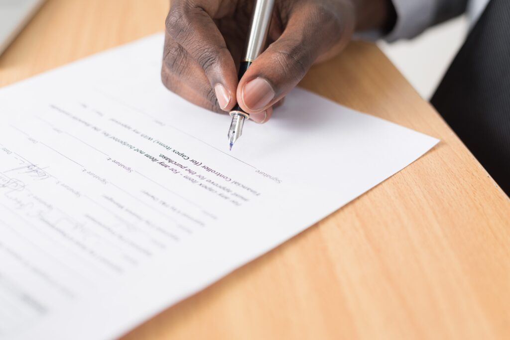Close up of right hand with pen signing a printed document.