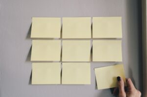 Nine sticky notes in a grid format on a wall, with one sticky note being put up by a hand