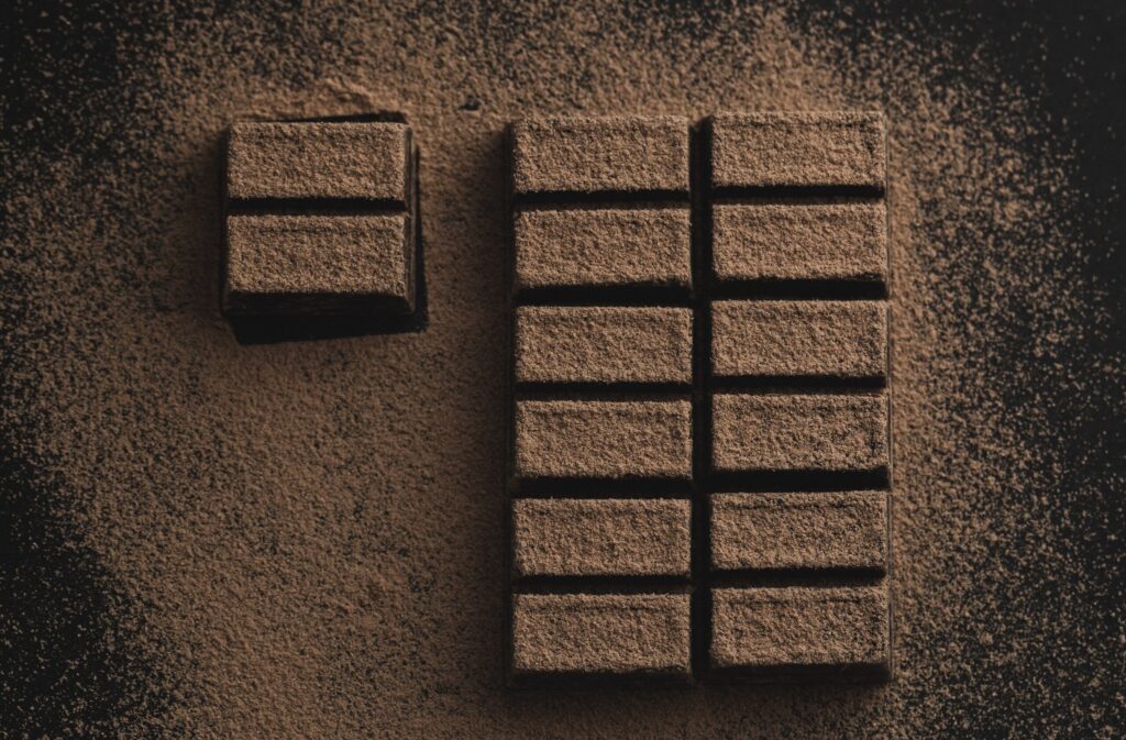 Chocolate bar dusted with chocolate. Two sections are on the left, and more sections of chocolate are on the right.