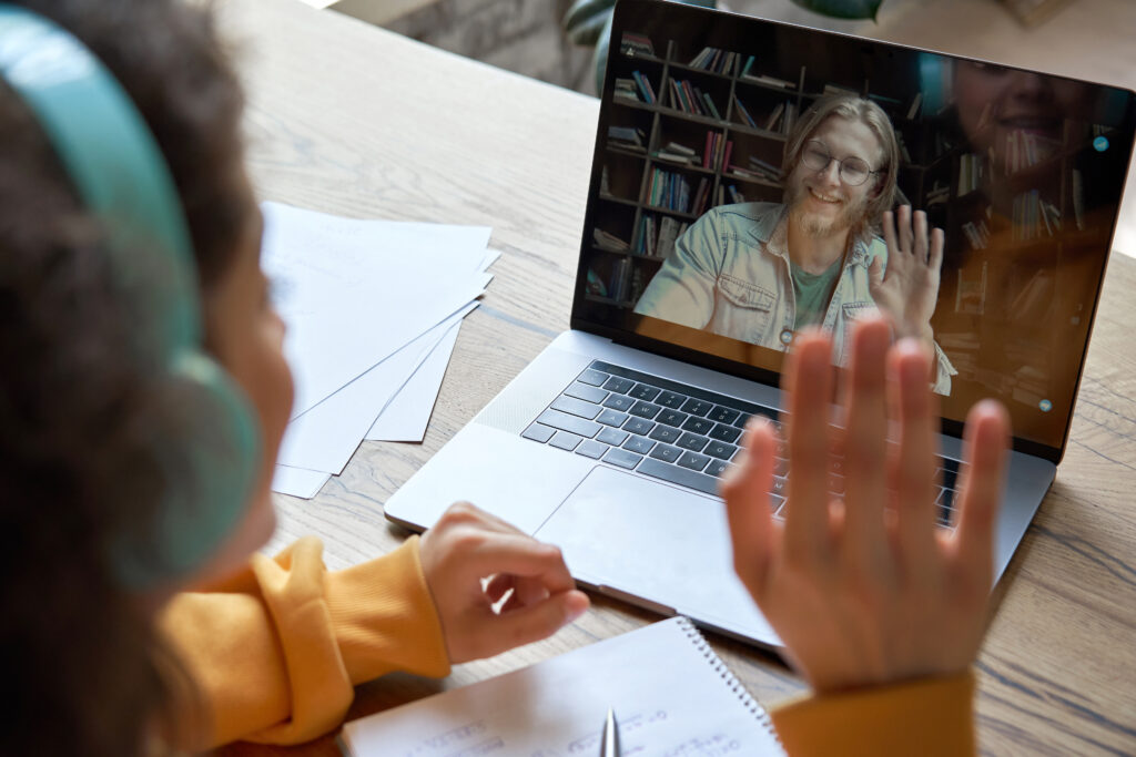 A student waving to an instructor on their laptop.