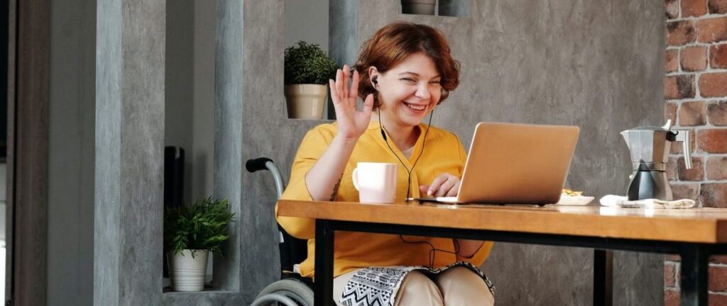 woman in a wheelchair saying hello in an online meeting