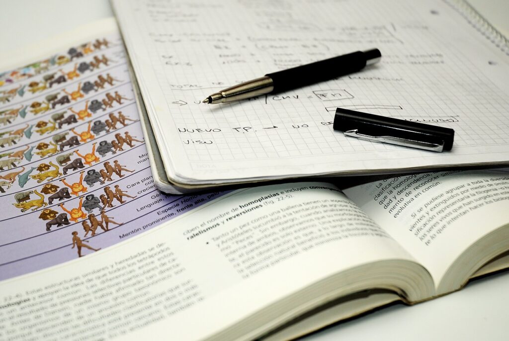a pen and filled notebook rest atop an open textbook.
