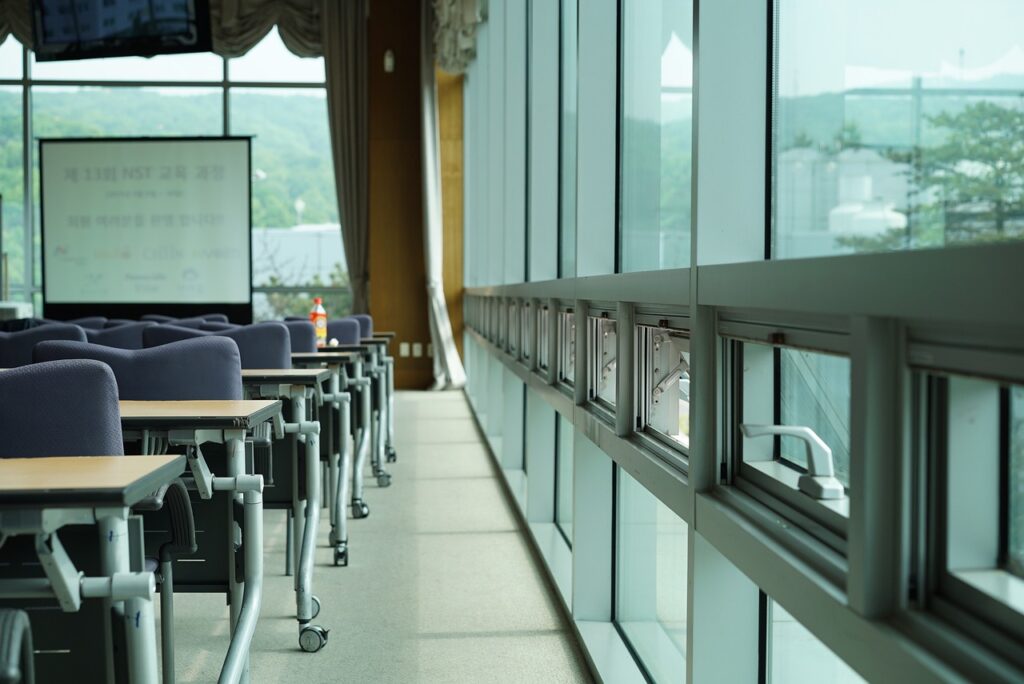an empty classroom, featuring numerous desks and a wall filled with windows.