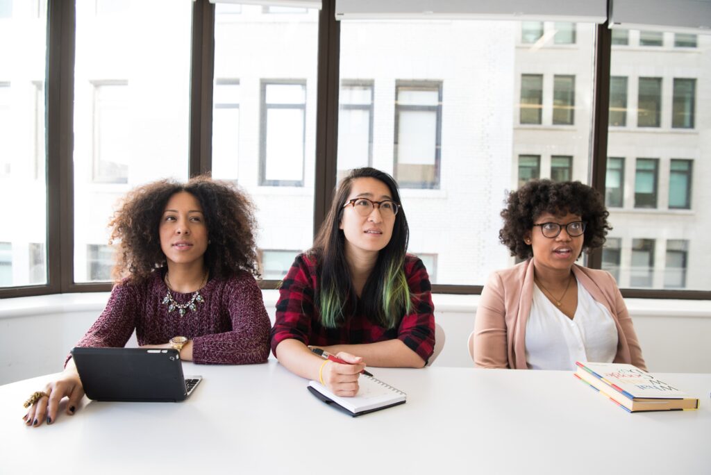 Three visible minority female students of sit and take notes