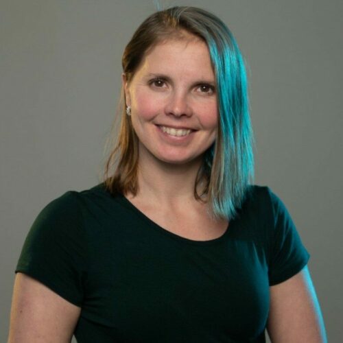 A woman smiling with a black shirt on and unique blue side-lighting