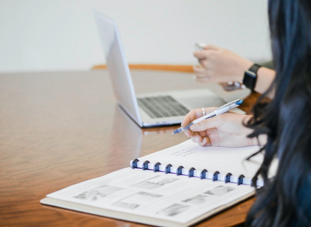 Students using a computer, holding a pen and writing in a book.